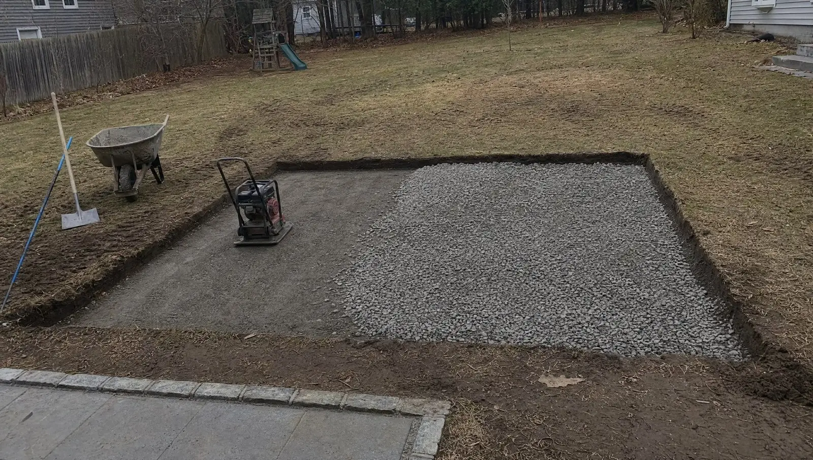 Excavated and compacted gravel base ready for a paver patio in a Connecticut backyard.