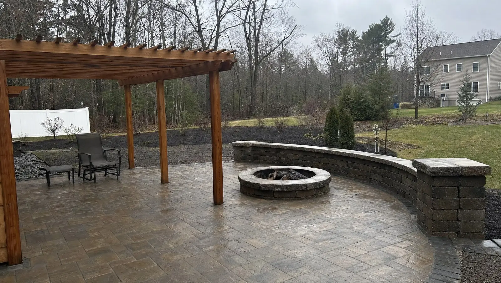 Finished backyard paver patio with a stone seating wall, fire pit and cedar pergola.