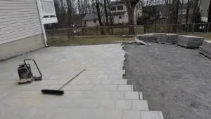 Paver patio job in a Connecticut backyard about two thirds laid, with the remaining gravel base still open.