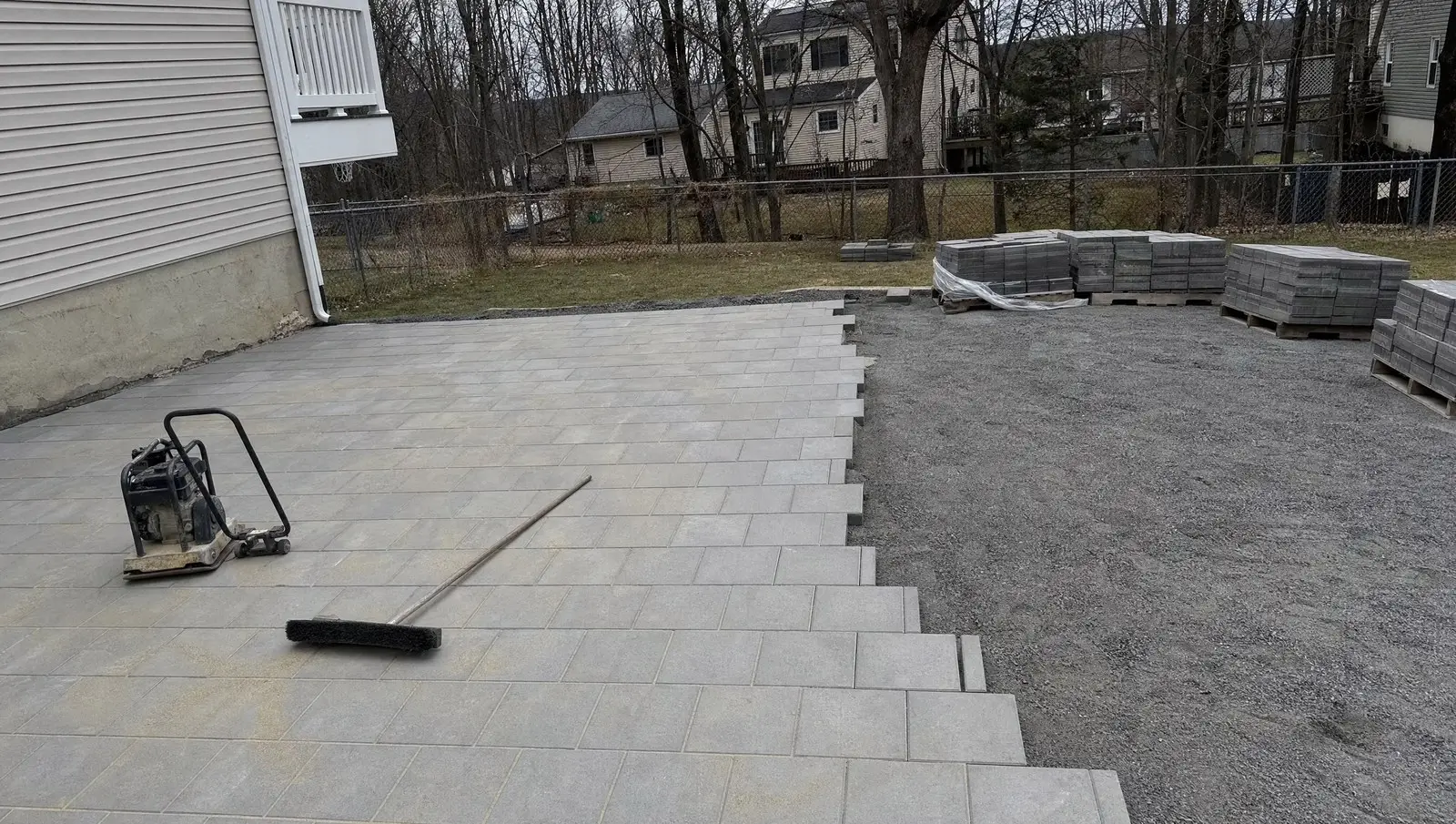 Paver patio job in a Connecticut backyard about two thirds laid, with the remaining gravel base still open.