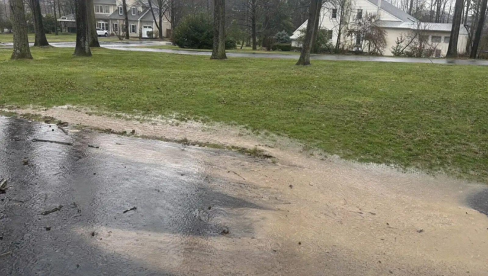 Runoff sheeting off a saturated lawn and pooling on a driveway after heavy rain.