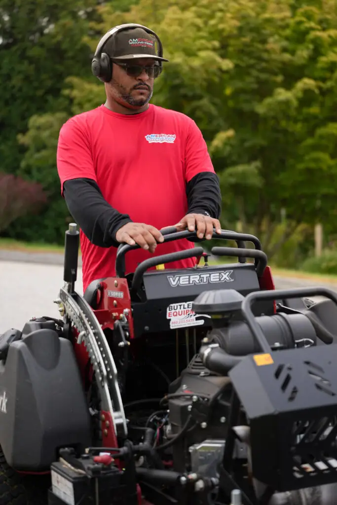 American Ground and Snow Management crew member on a stand-on mower during weekly lawn care in Groton CT