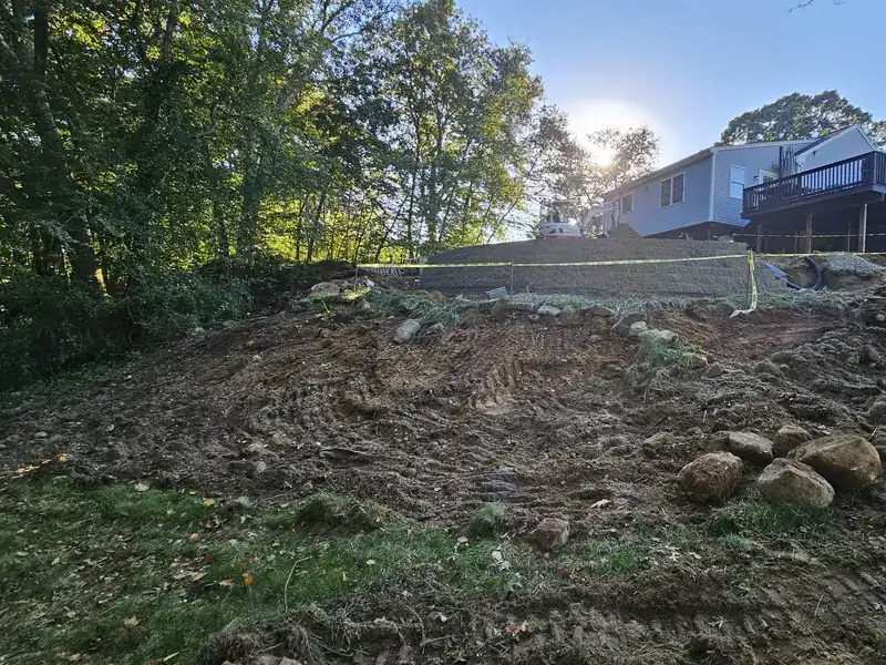 Backyard slope before AGSM regrading: torn up, uneven ground with rocks below a deck