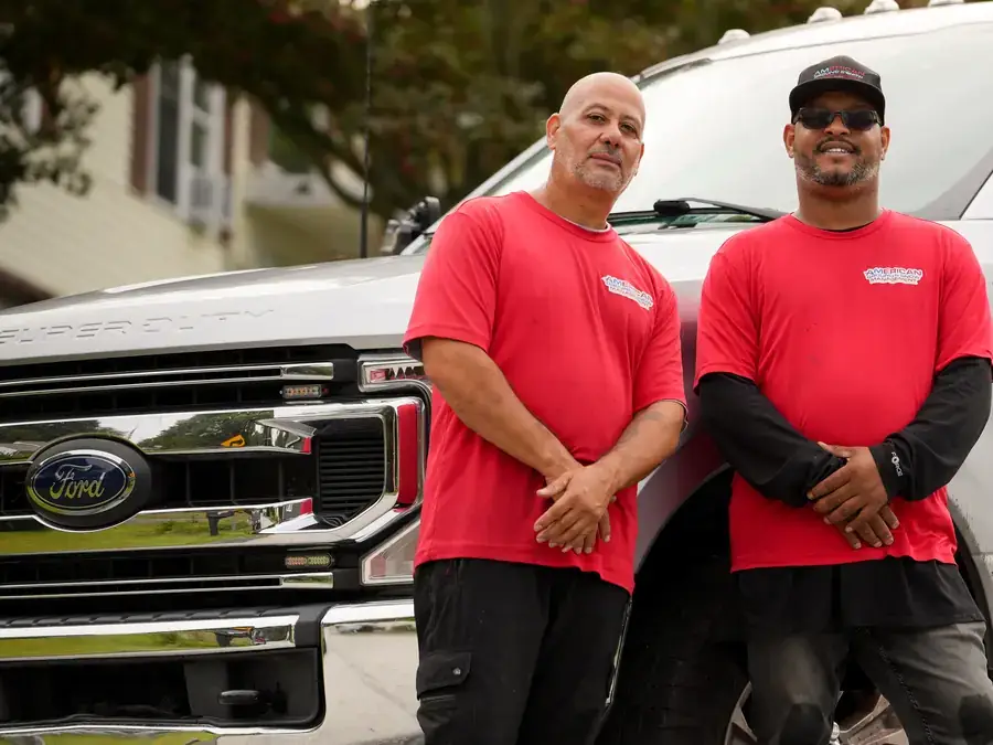 Two American Ground and Snow Management crew members standing by their company truck