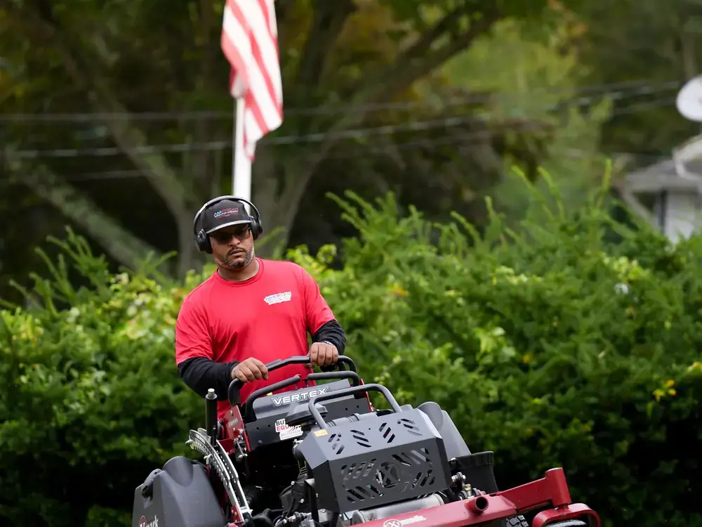 American Ground and Snow Management crew member mowing a lawn in front of an American flag